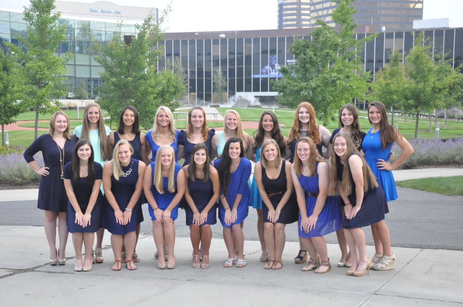 A group of Kappa Beta Gamma sorority members from Lawrence Technological University gather on the campus quad, smiling and posing together in blue dresses.